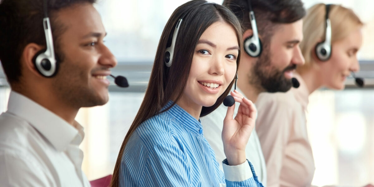 Center with colleagues. Side view of line of call centre employees with focused smiling asian girl smiling with manager.
